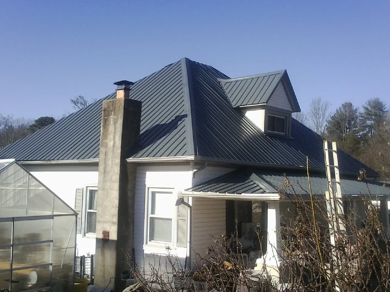Dark blue standing seam metal roof on a white farmhouse with dormer in Dickinson