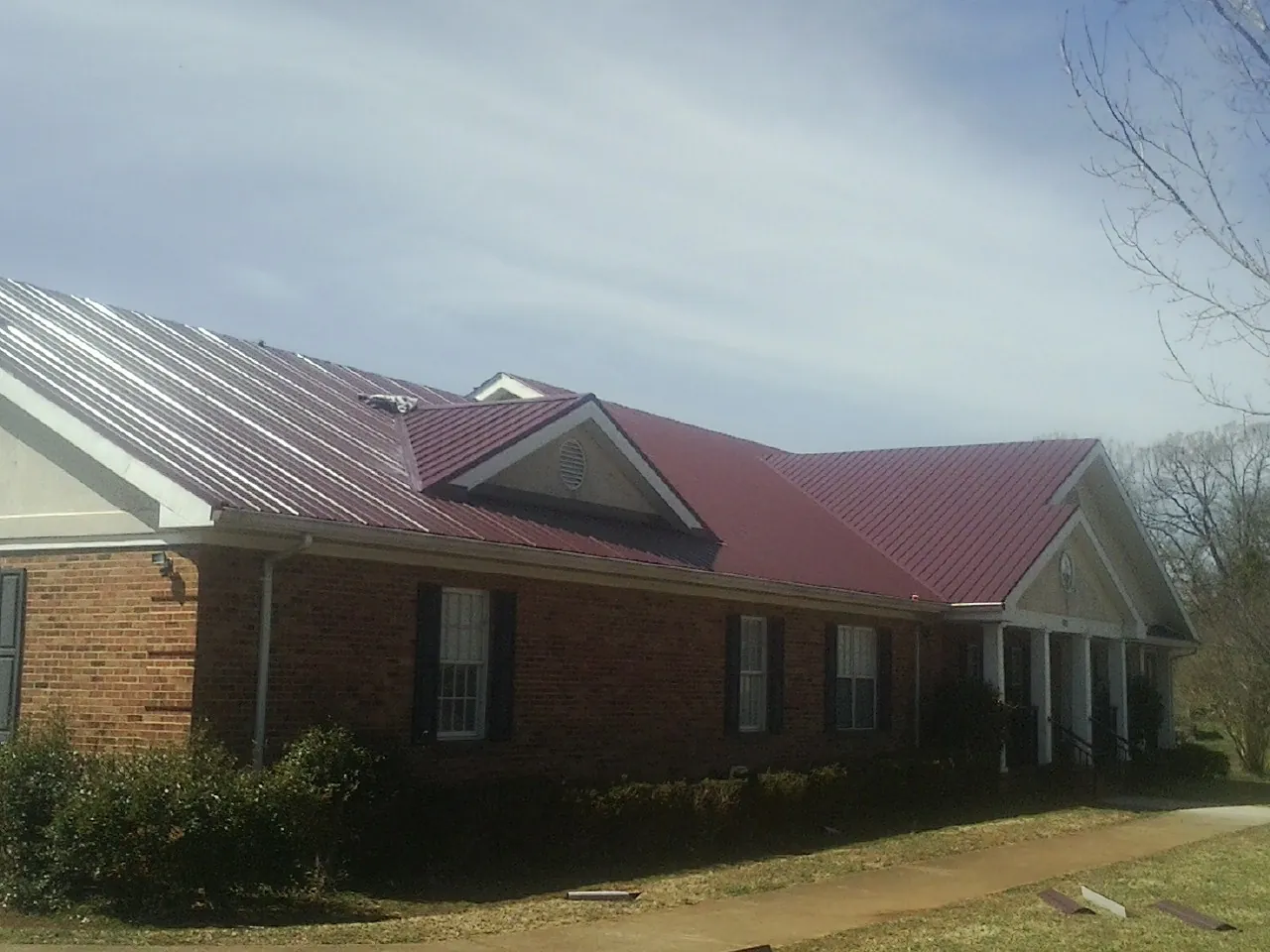 Red metal roof with gabled entries on a long brick building, from a Hail Damage Roof Repair job in Dickinson