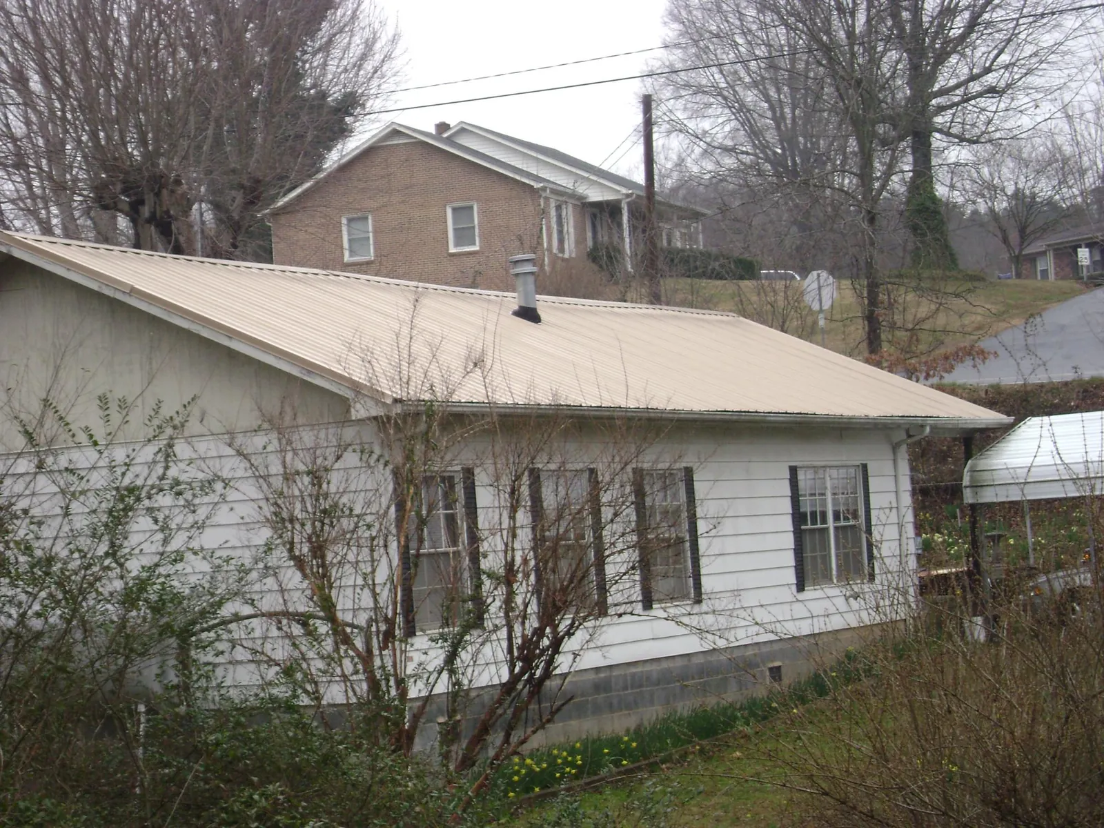Tan metal roof on a white sided house set into a hillside — Commercial Roofing by Roofing Brothers in Dickinson